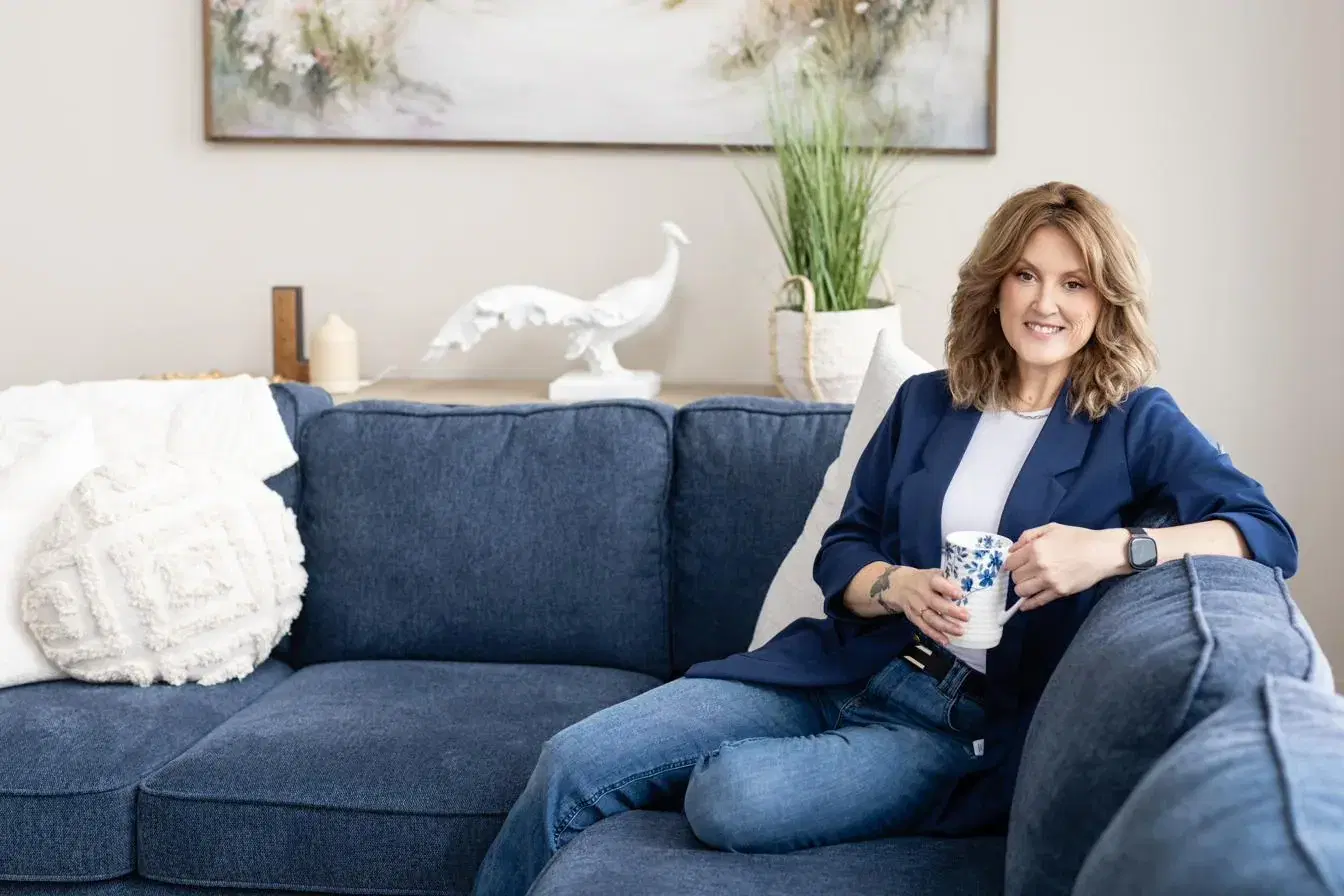 Angela Fawcett, MSW, RSW, relaxed on a navy couch with a cup of tea